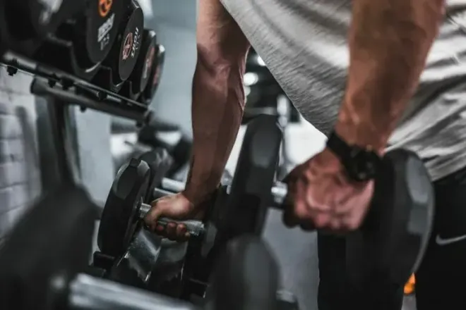 A person reaching for a dumbbell on a gym rack to begin a workout.