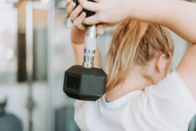 A person performs a dumbbell overhead tricep extension behind their head while in a gym setting.