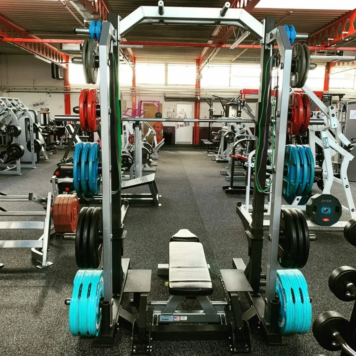 A gym power rack with an adjustable weight bench, surrounded by various weight plates in a gym setting.