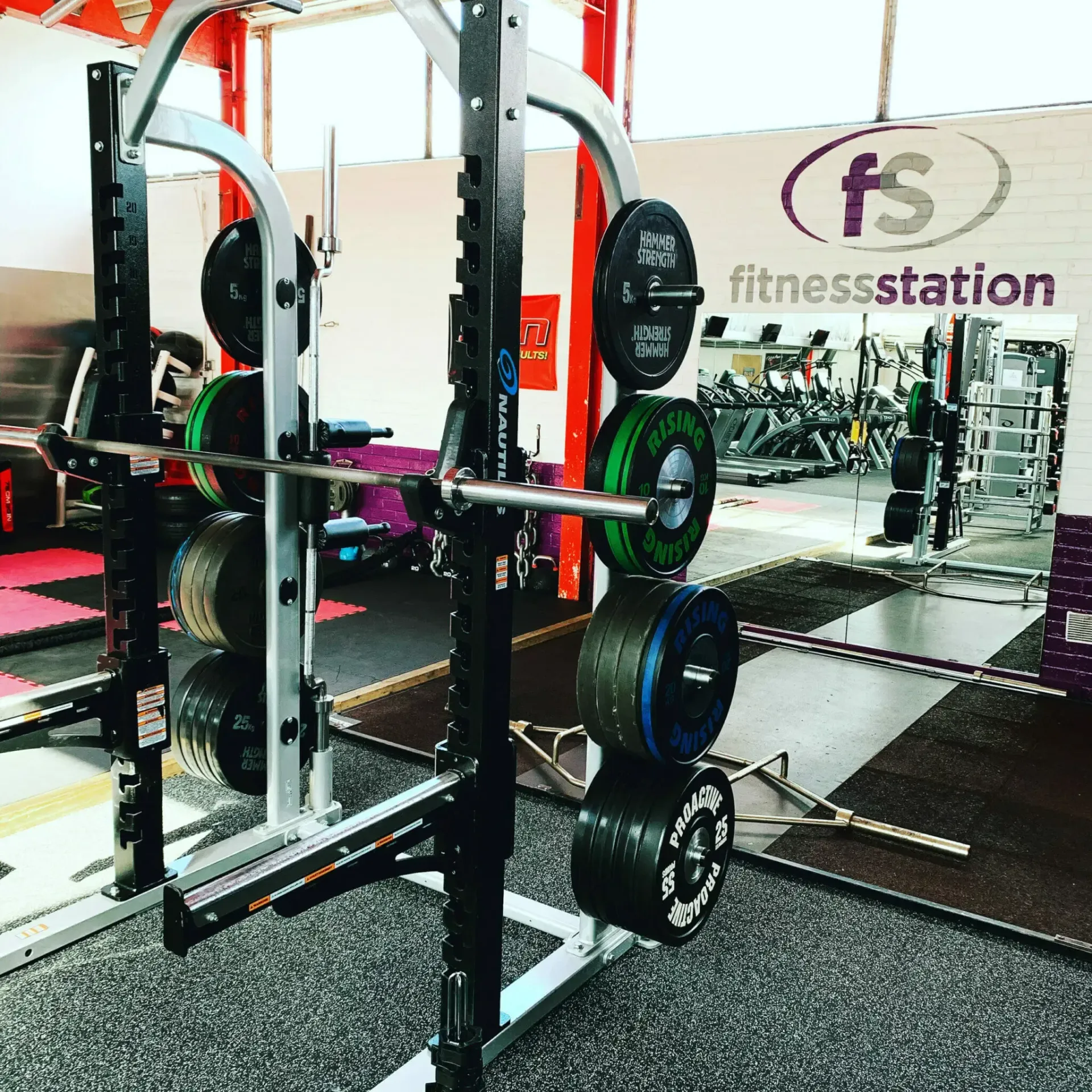 A squat rack with weight plates stored on the side in a gym with a 