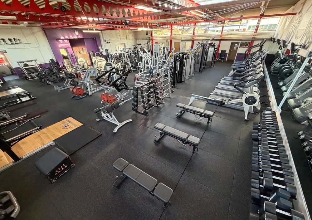 High-angle view of a well-equipped gym featuring rows of exercise machines, weight benches, and dumbbells on a black floor.