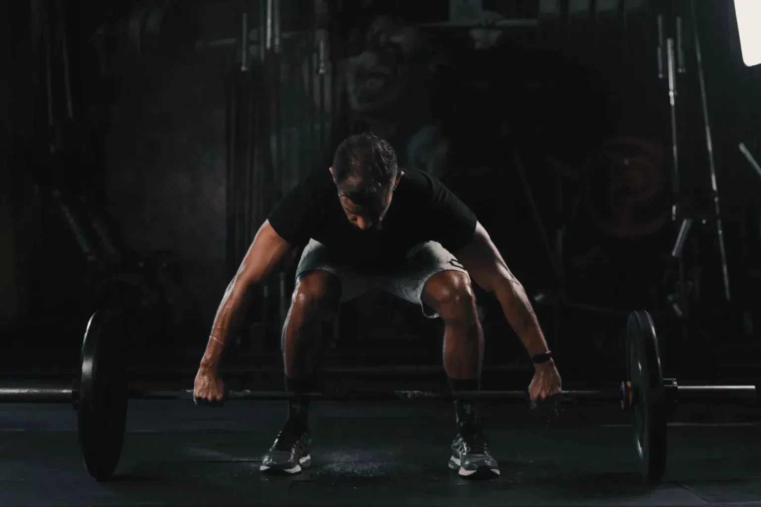 A person in a gym setting preparing to lift a barbell from the floor, hands gripping the bar with a neutral posture.