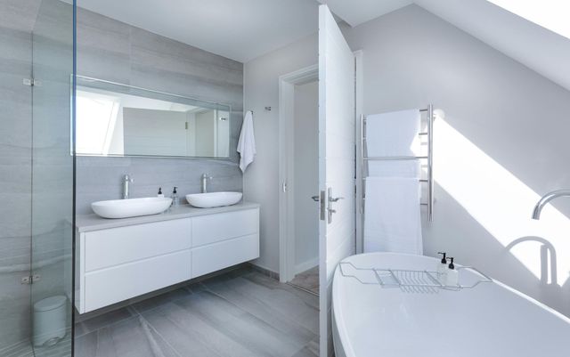 Modern white bathroom with double sink vanity, soaking tub, and heated towel rack.