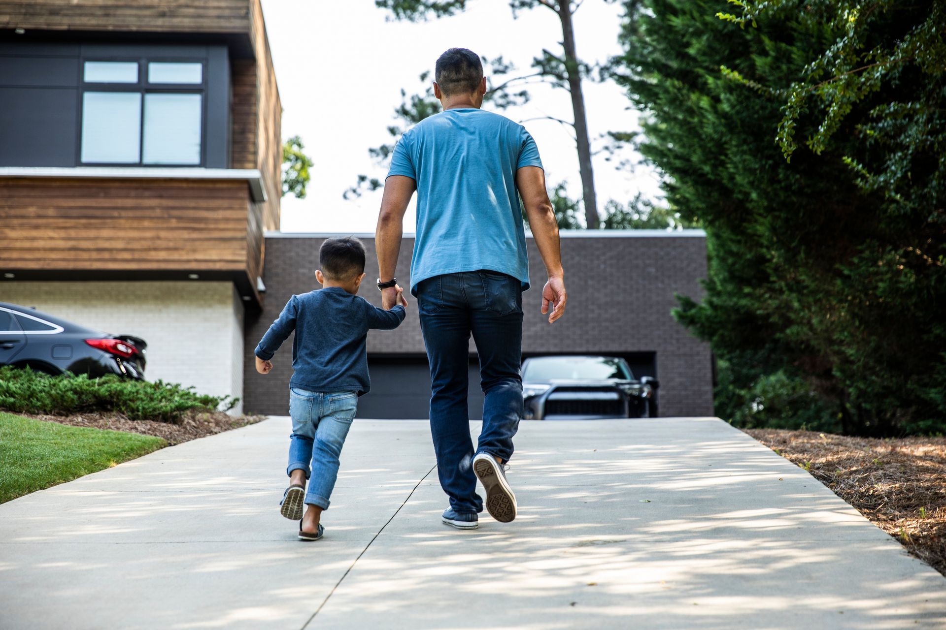 A man and a child are walking down a sidewalk holding hands.