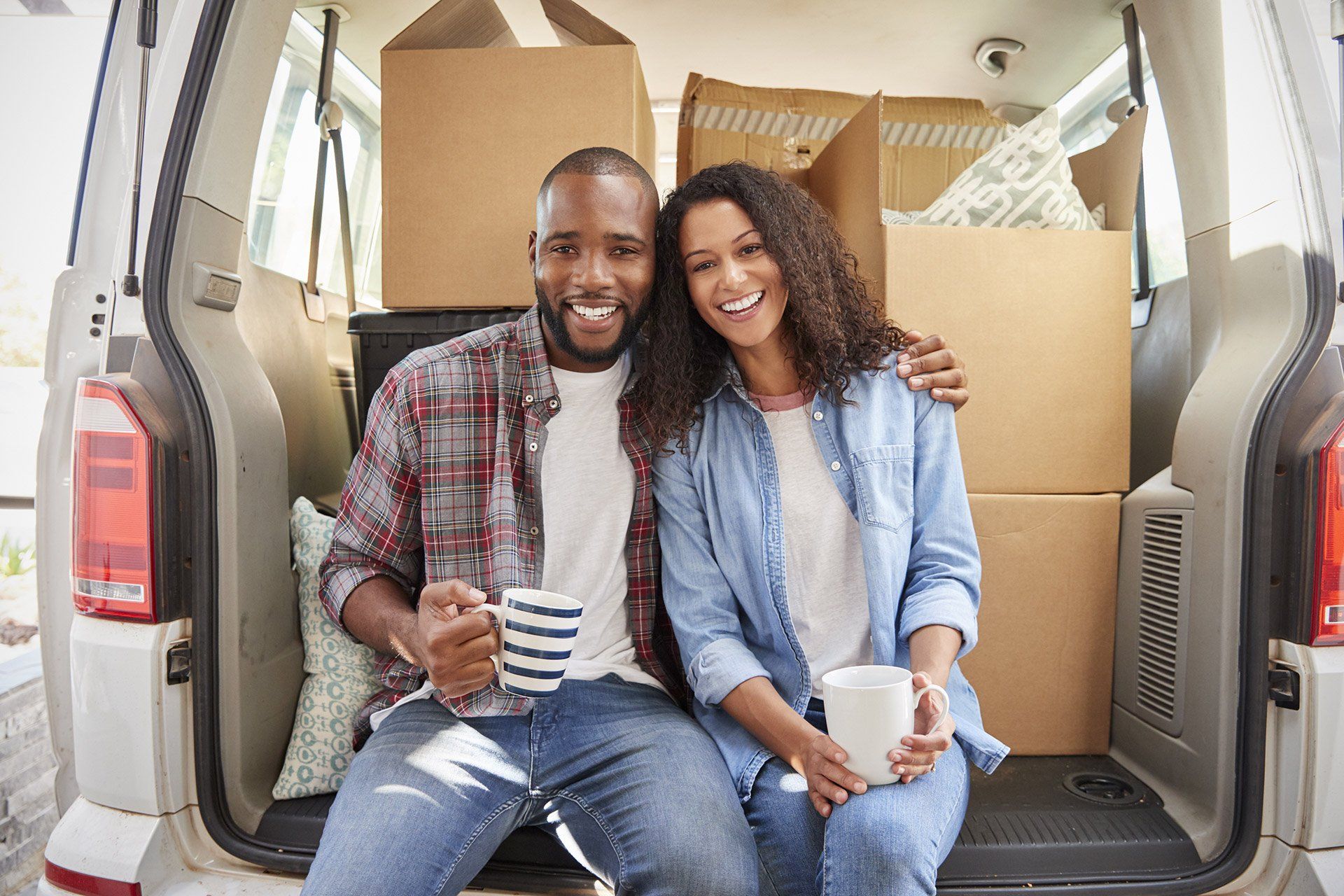 couple, smiling, sitting in back of vehicle with boxes inside