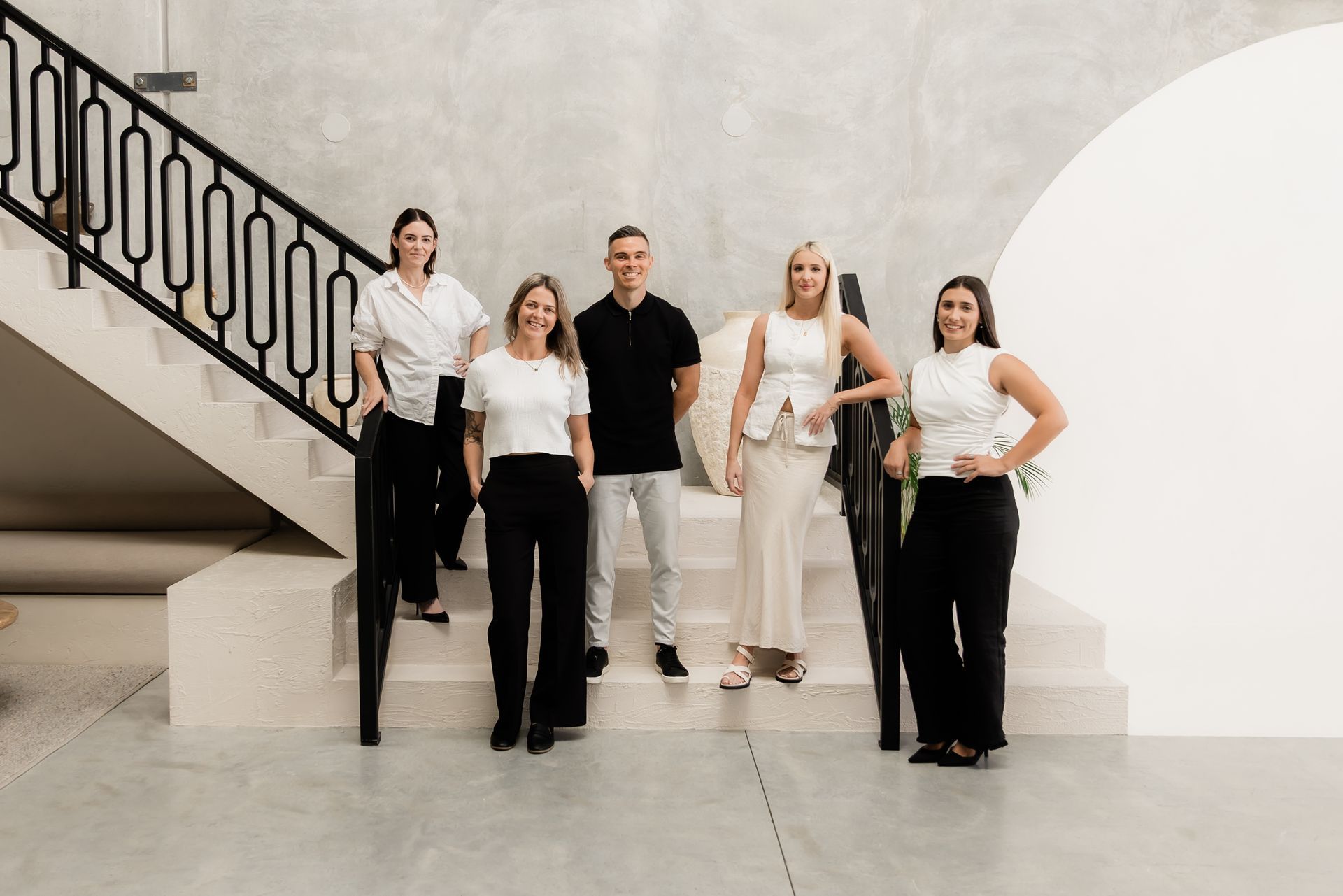 Five people posing on a modern staircase; neutral tones; well-dressed; looking at the camera.