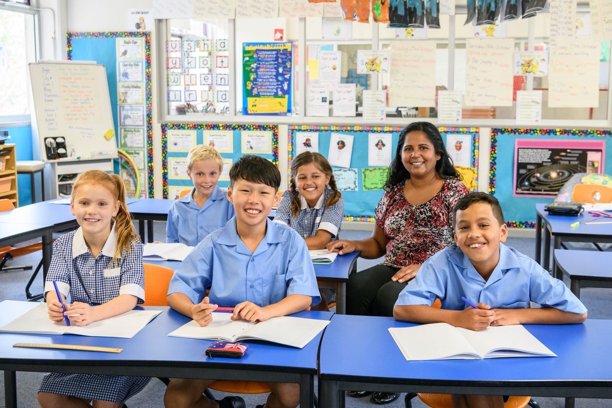 A group of children are sitting at desks in a classroom with their teacher.