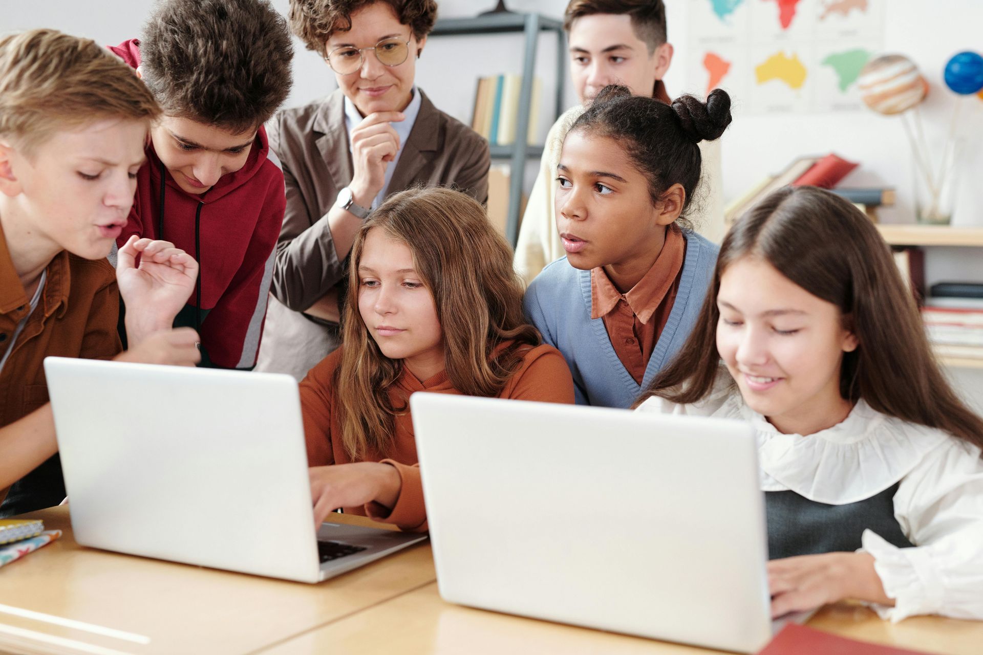 Students and a teacher looking at laptops in a classroom, focused on the screens.