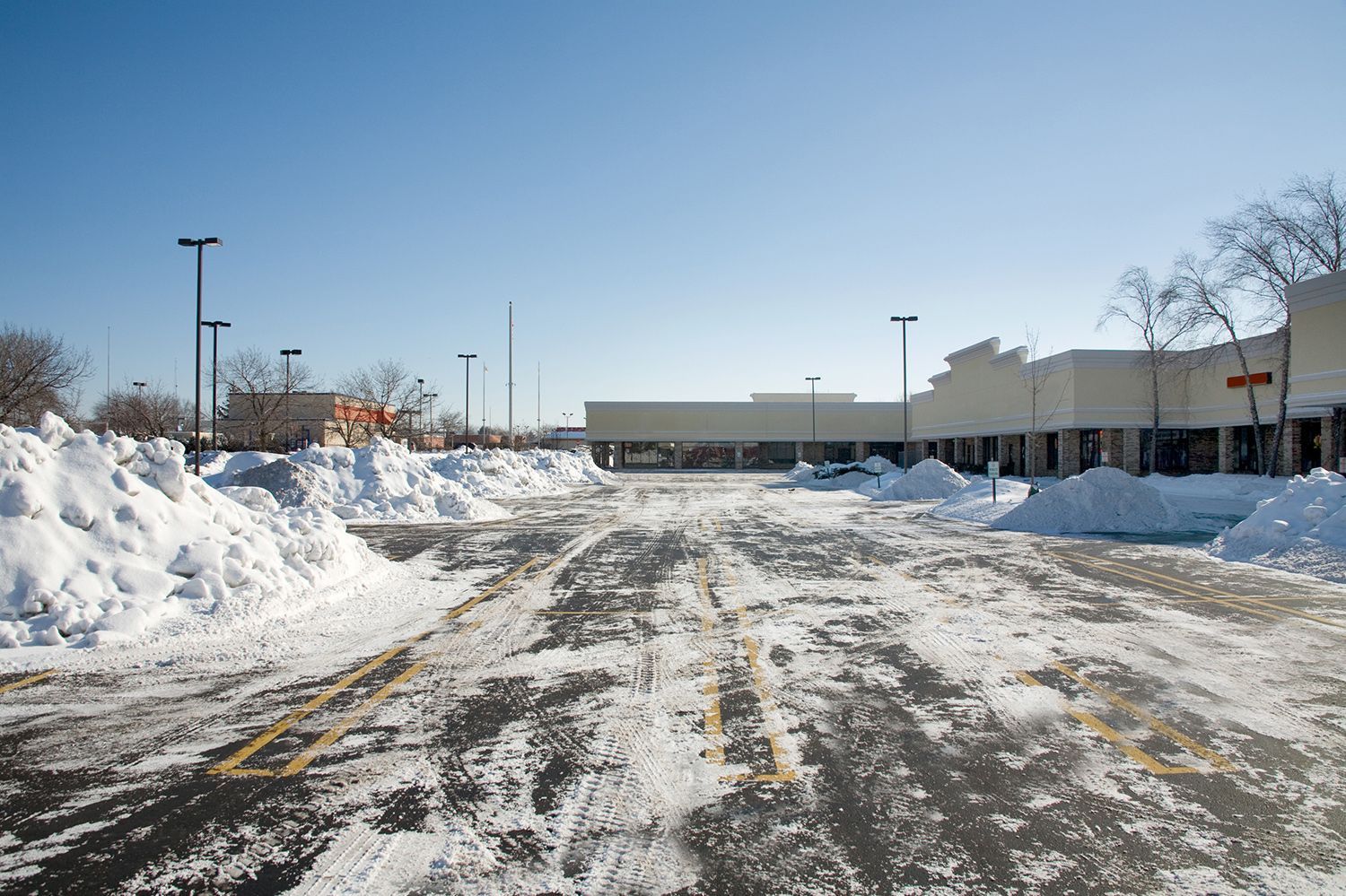 A snowy parking lot with a building in the background