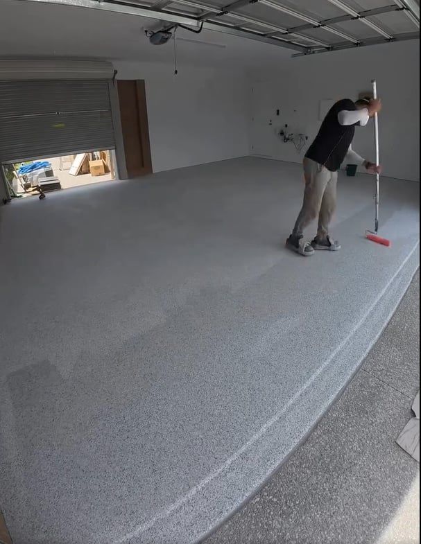man using roller to spread epoxy floor paint throughout garage