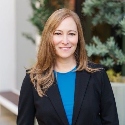 A woman in a black jacket and blue shirt is smiling for the camera.