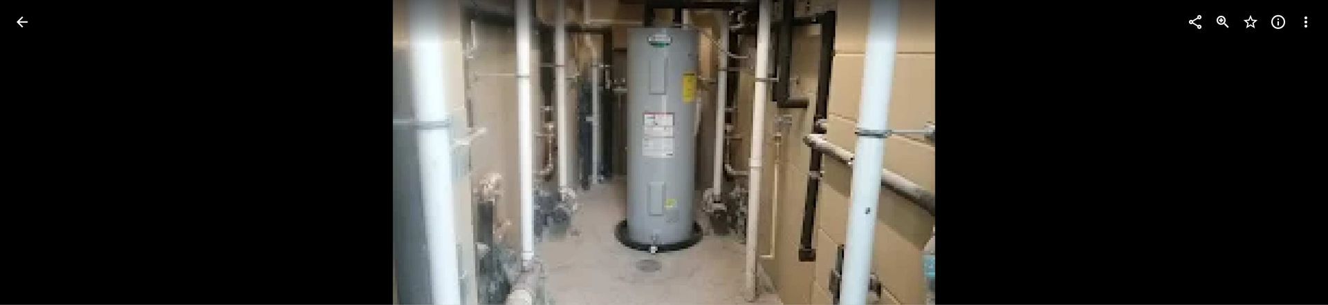 A professional technician in a blue uniform working on a silver wall-mounted tankless water heater indoors.