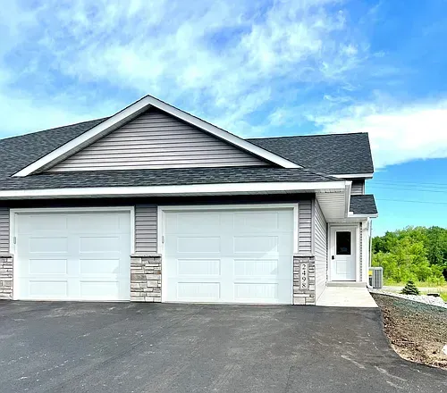 Two-car garage with gray siding, stone accents, and a white door under a blue sky.