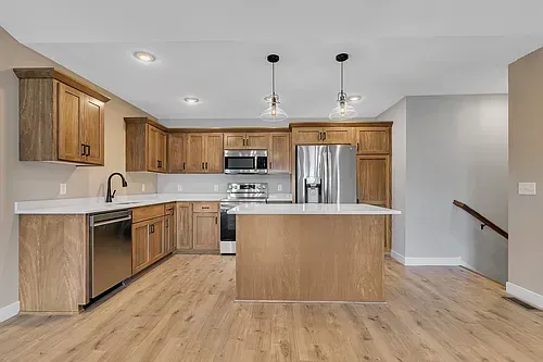 Modern kitchen with wooden cabinets, stainless steel appliances, and white countertops.