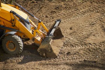 Yellow backhoe digging in brown dirt, leaving tire tracks.