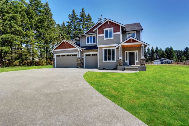Two-story house with gray siding, brown trim, and a concrete driveway. Green lawn, blue sky.