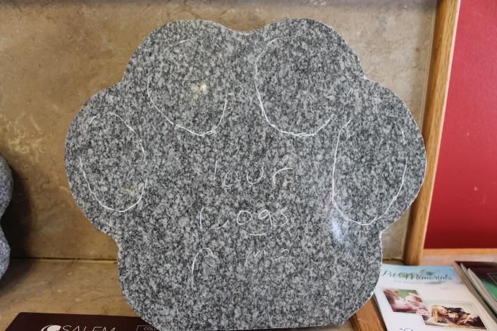Gray flower-shaped stone plaque displayed on a shelf, with faint white vein lines.