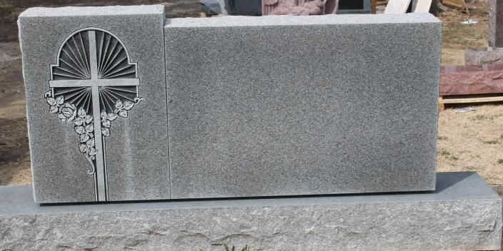 Gray granite cemetery headstone with a carved cross and floral design on the left side