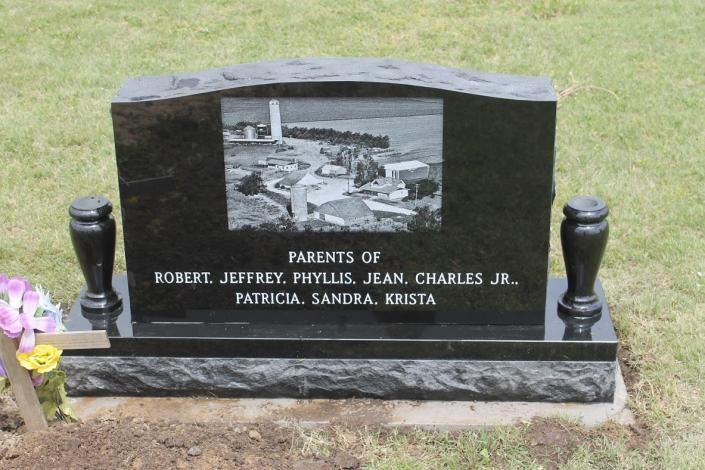 Black granite memorial headstone with an inset photo and engraved names in a grassy cemetery.