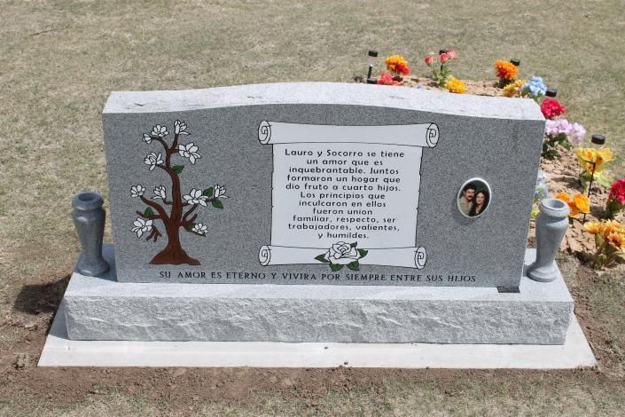 Gray memorial headstone with floral engravings and flowers on top in a cemetery