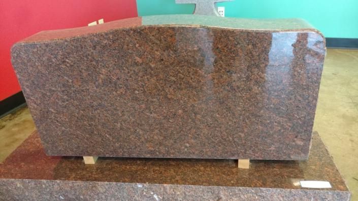 Large polished brown stone slab on a wheeled platform in a warehouse-like setting