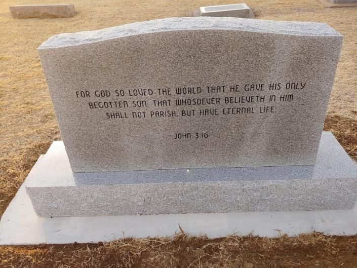 Gray granite memorial marker on a white base in a dry cemetery setting.