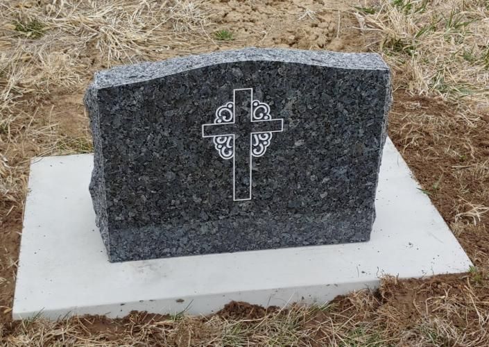 Gray granite memorial stone with engraved cross on a white base in dry grass