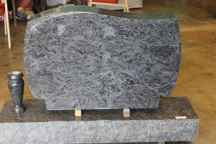 Gray granite headstone on a stone base, with a small decorative urn beside it in a workshop or showroom