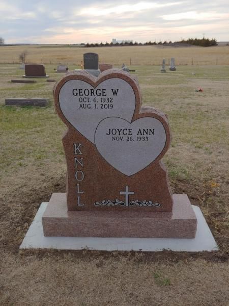 Heart-shaped double gravestone in a grassy cemetery under a cloudy sky.