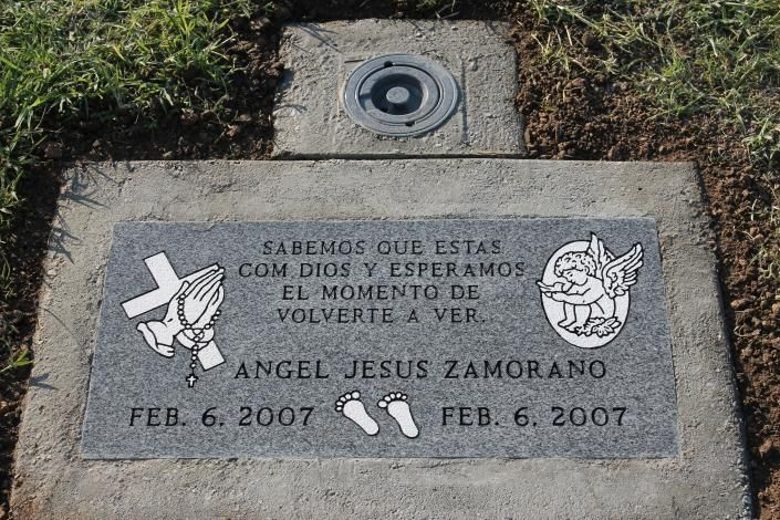 Concrete memorial plaque with Spanish text and footprints in a grassy outdoor area.