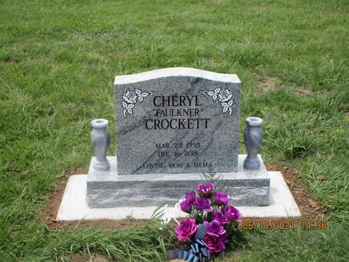 Gray headstone with purple flowers on a grassy grave plot