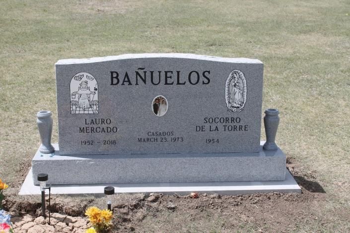 White gravestone for the BAÑUELOS family in a cemetery, with flowers at the base.