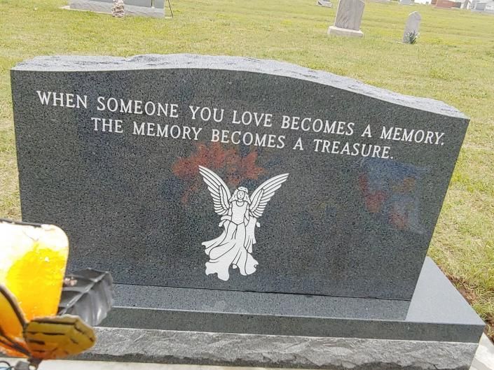 Black granite memorial headstone with angel and engraved tribute in a cemetery.