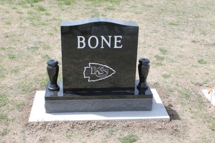 Black gravestone engraved “BONE” with a sports team logo, set on grass.