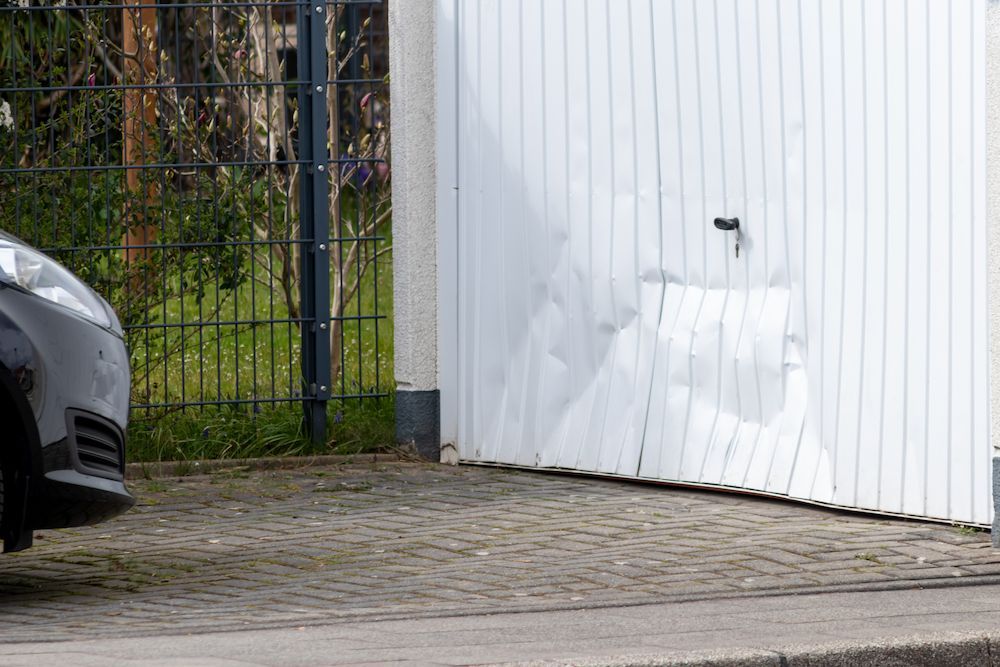 A Car Is Parked in Front of A Damaged Garage Door.