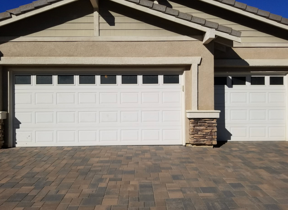 A House with Two White Garage Doors and A Brick Driveway