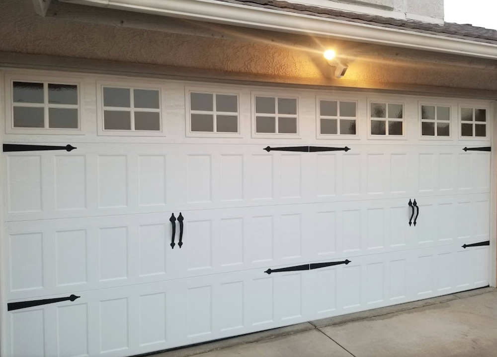 A White Garage Door with Black Handles and Windows on A House.