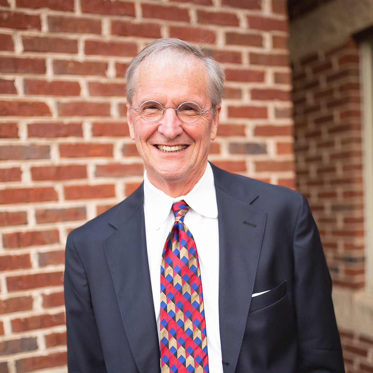 Man in suit and tie smiles in front of a brick wall.
