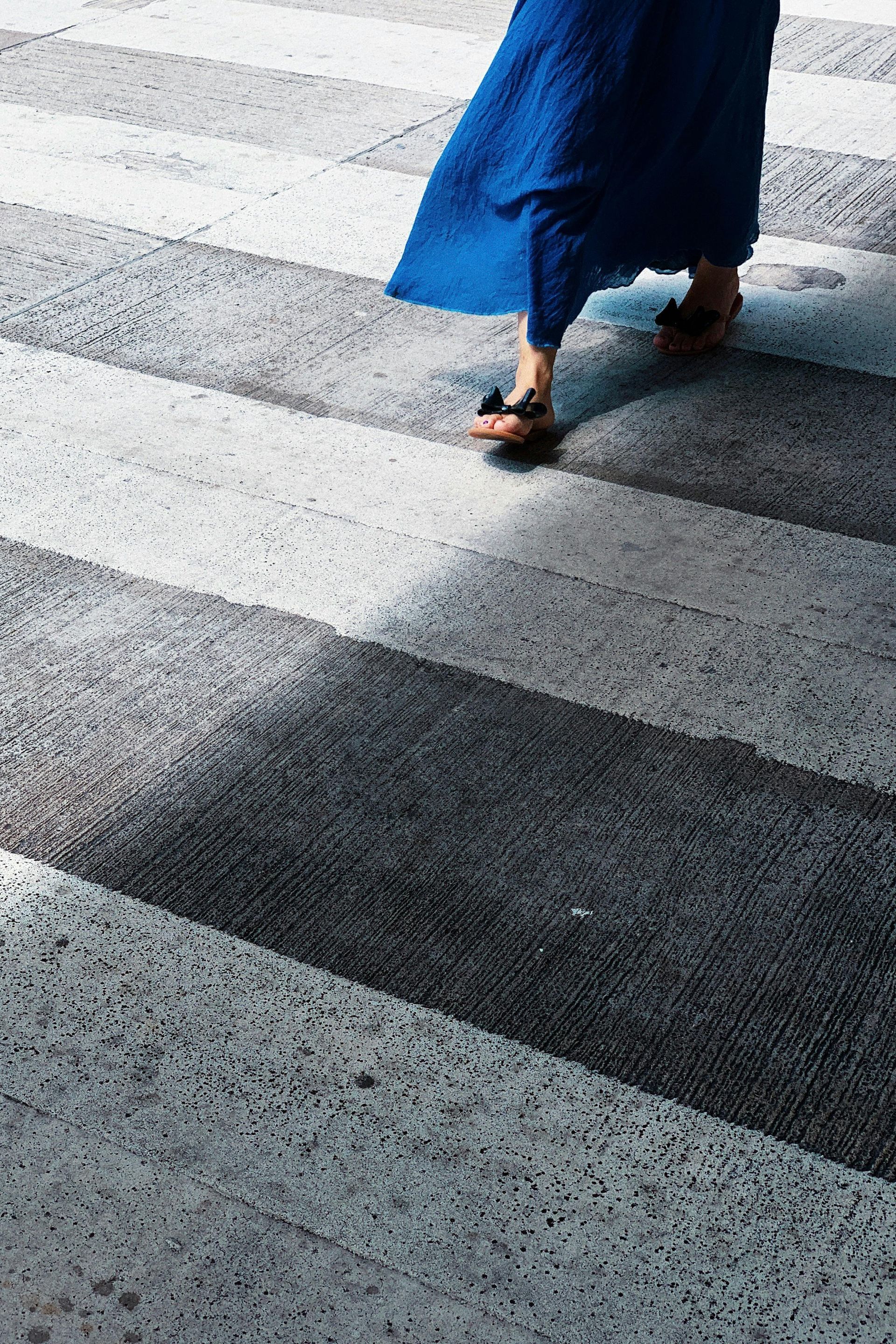 Person in a blue dress and sandals walks across a crosswalk with black and white stripes.