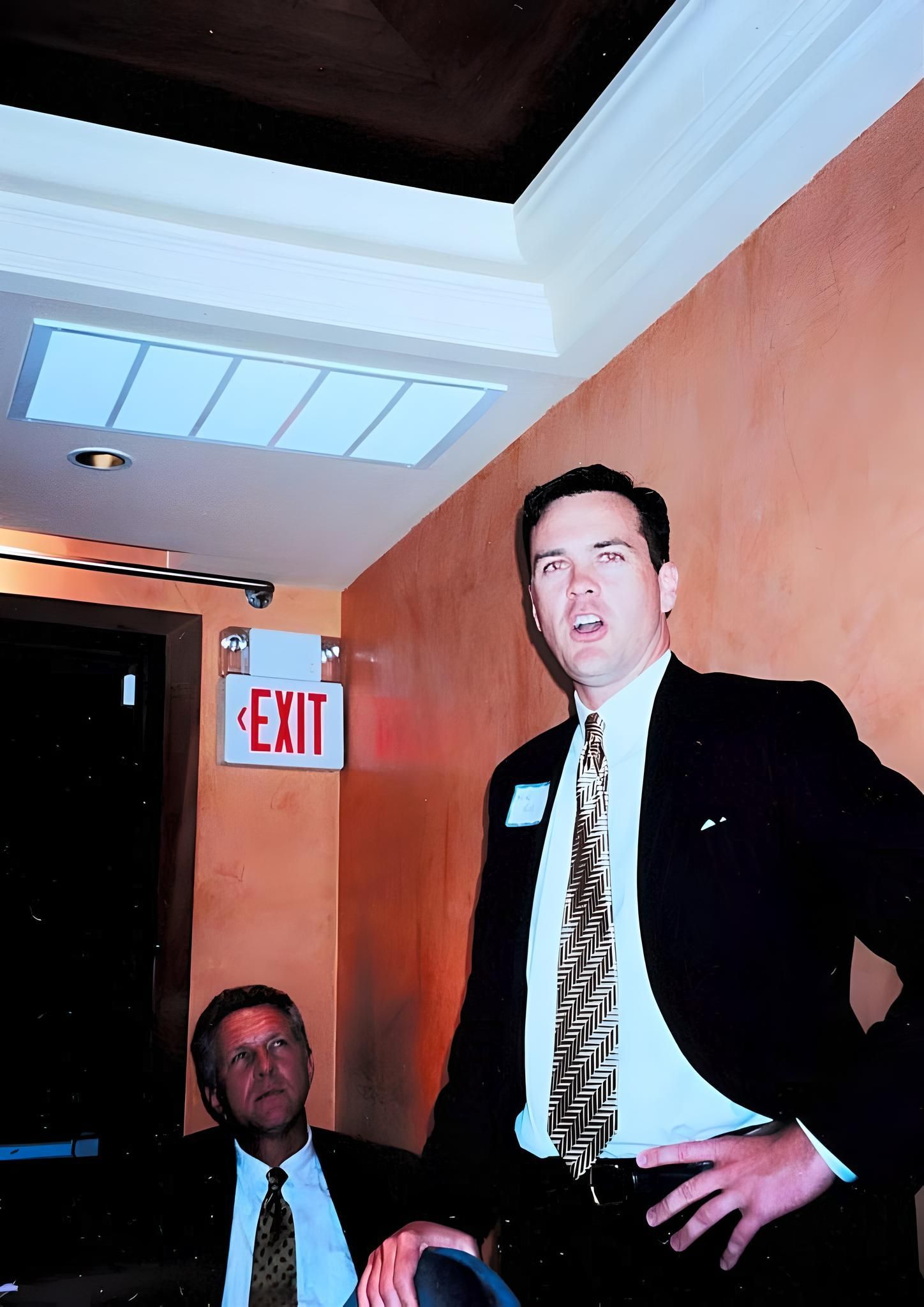 A man in a suit stands in front of an exit sign at J.F. Kelly Inc. company party
