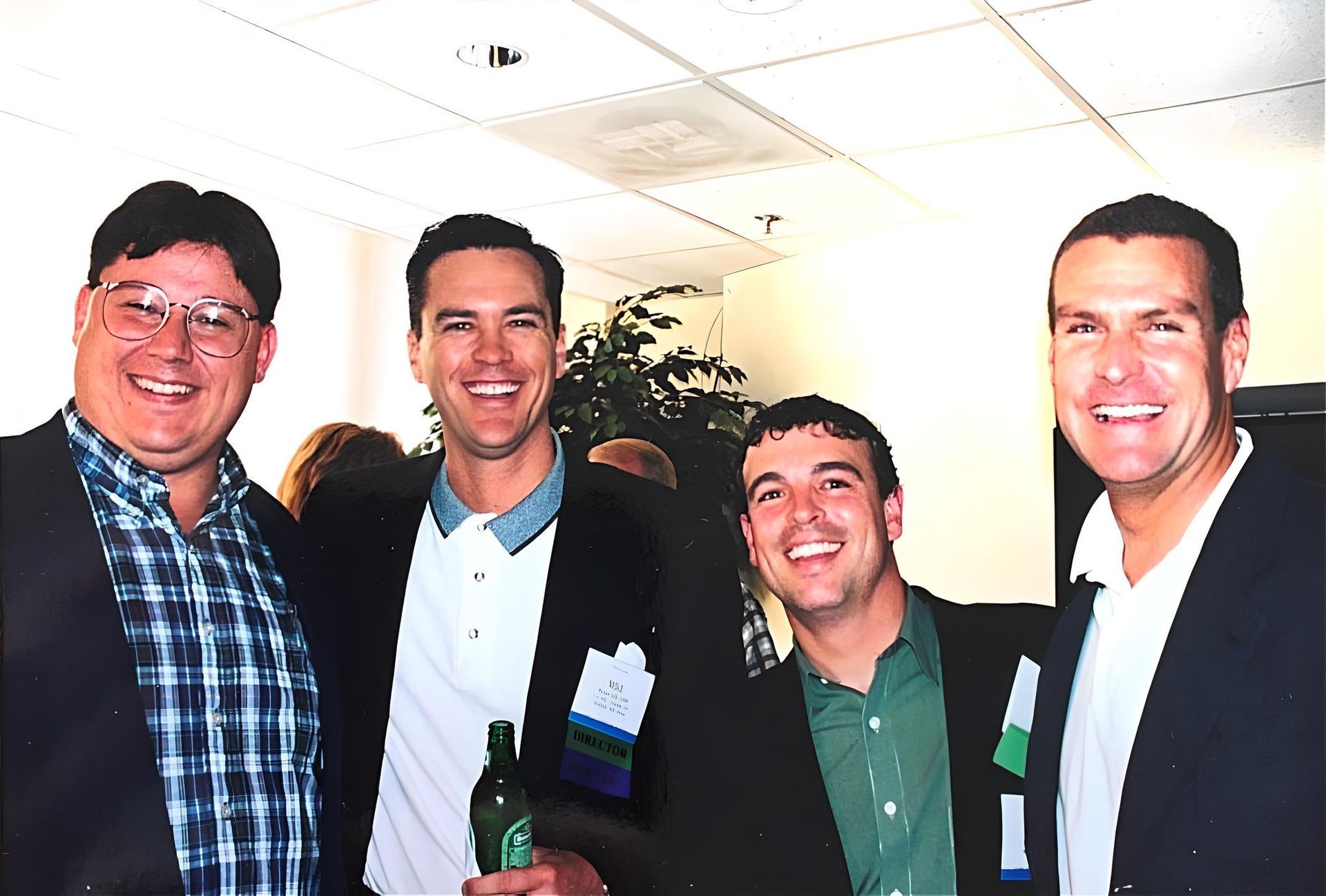 Four men posing for a picture with one holding a bottle of beer at J.F. Kelly Inc. company party