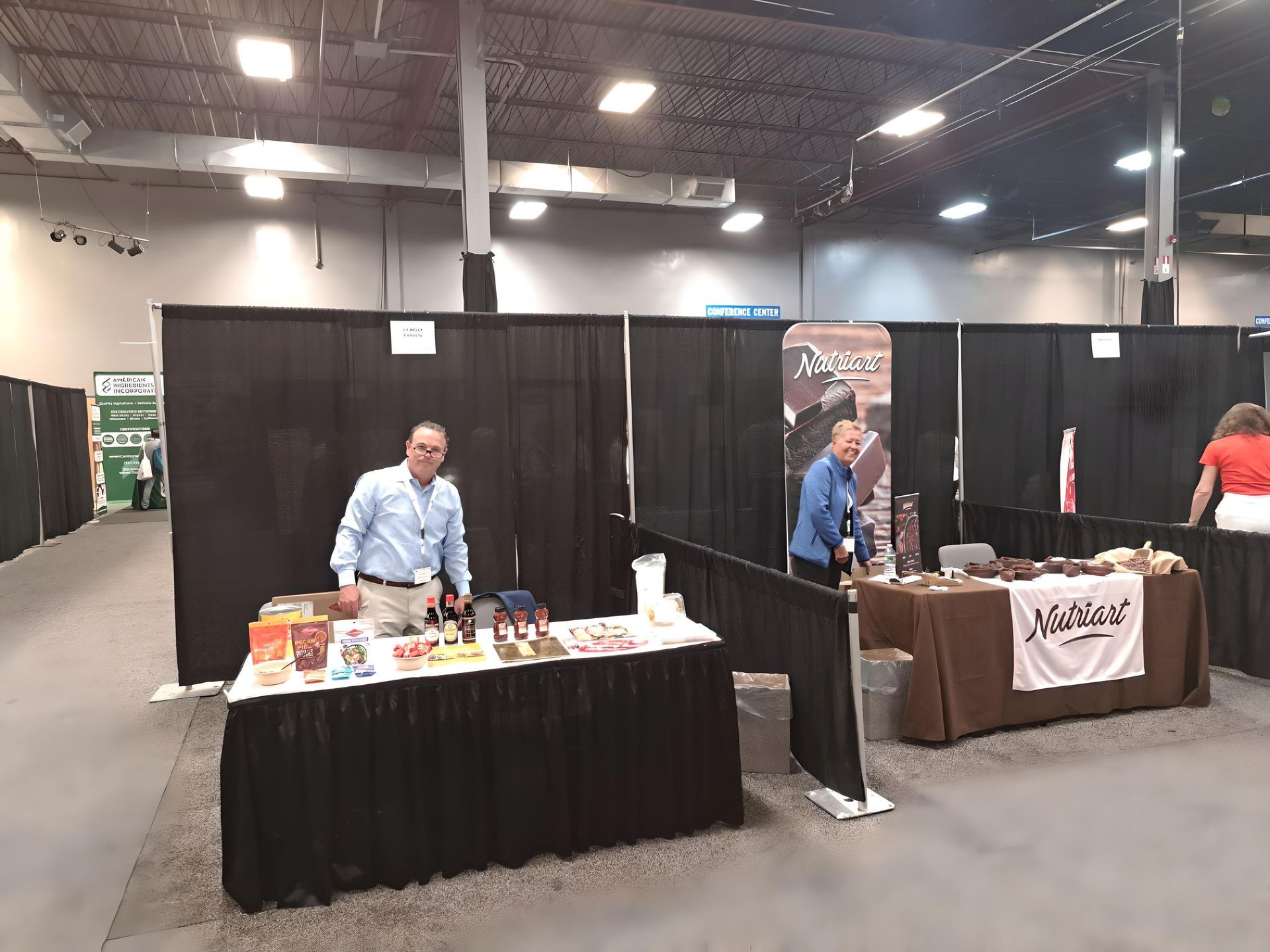A man is standing in front of a table at a food ingredient supplier convention