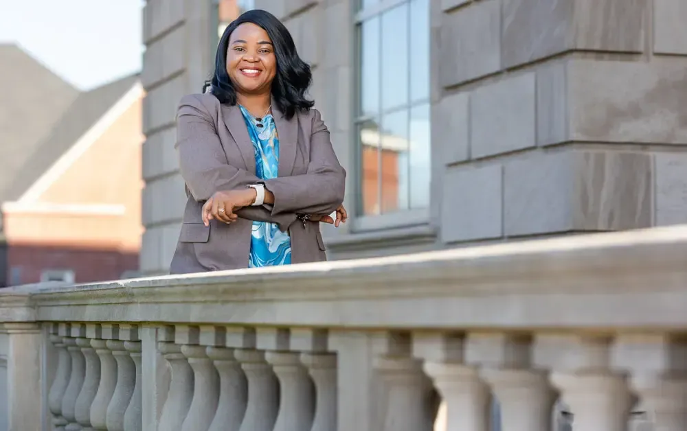 A woman in a suit is standing on a balcony with her arms crossed.