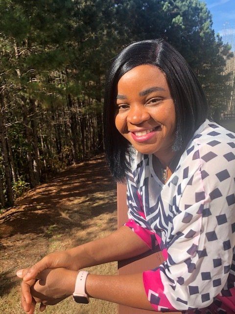 A woman is sitting on a bench in front of a forest.