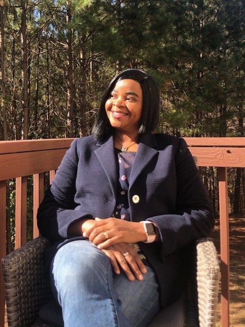 A woman in a blue jacket is sitting in a chair on a deck.