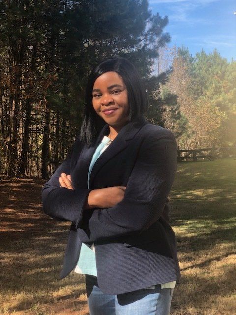 A woman is standing in a field with her arms crossed.