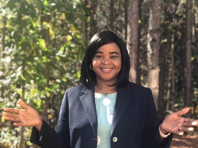 A woman in a suit is standing in the woods with her arms outstretched.