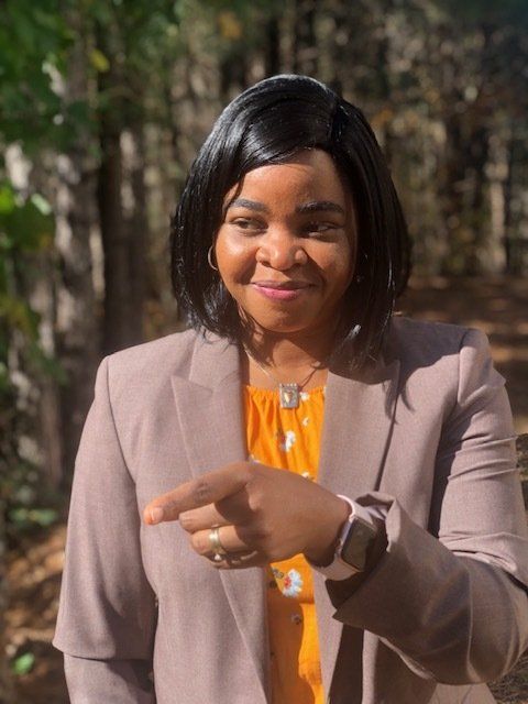 A woman in a suit is pointing at the camera.