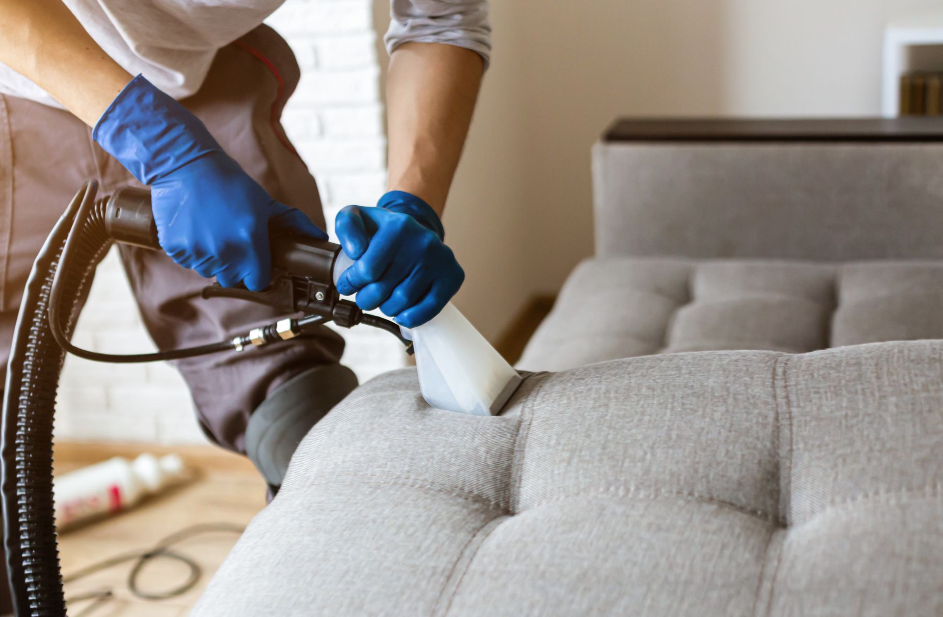 Professional sofa upholstery cleaning using a steam extraction tool on a gray fabric couch.