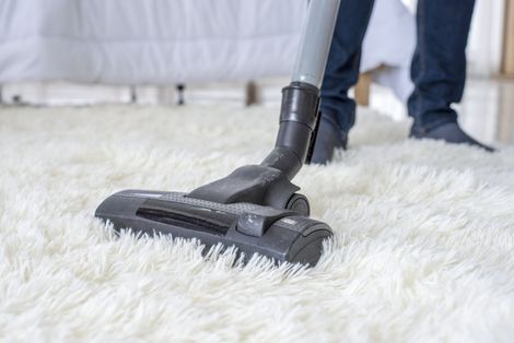 Person vacuuming a fluffy white rug with a grey vacuum cleaner.
